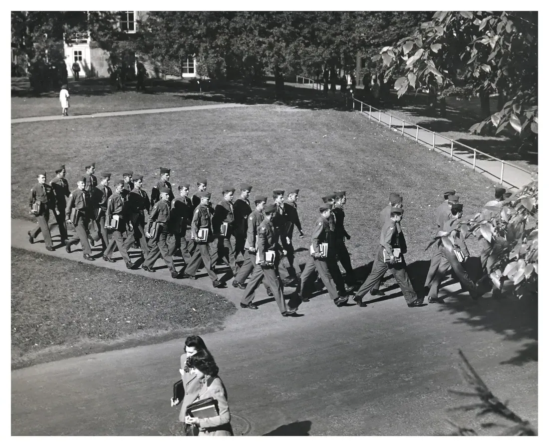In an archival photo dating to WWII era, a group of soldiers walk across campus.