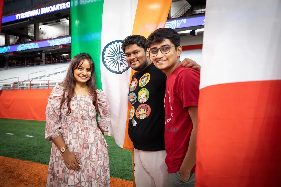 Three international students stand by international flags and smile.