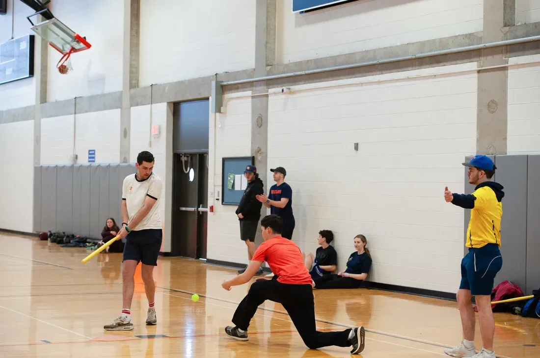 Students playing wiffleball in the gym.